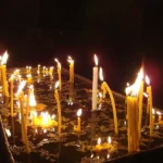 Many lit votive candles glowing in a dark church
