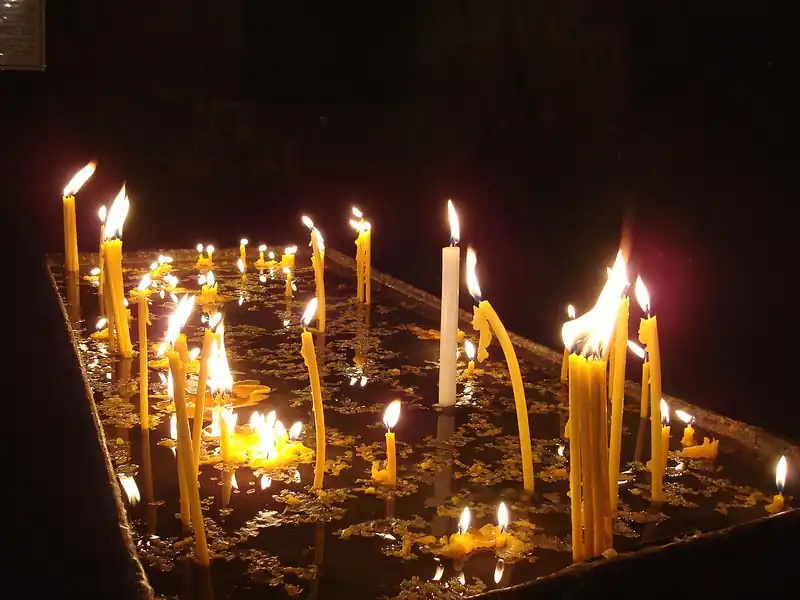 Many lit votive candles glowing in a dark church