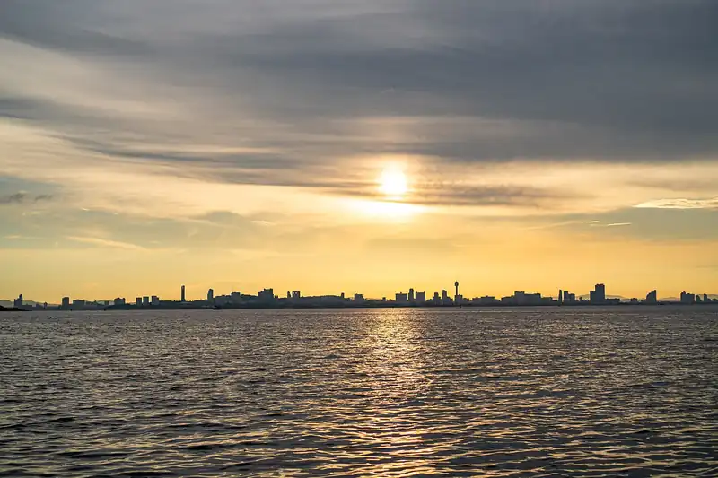 Sunset light reflecting on calm sea water with a distant city skyline