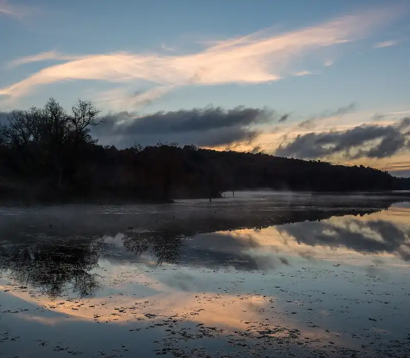 Mist over a calm lake at dawn with pink clouds reflected in the water